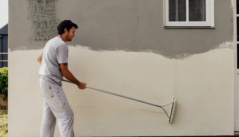 Stukadoor zet zandkleurig buitenpleisterwerk op de muur van een bungalow
